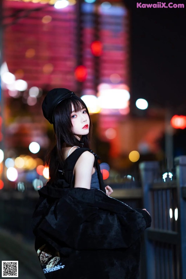 A woman in a black dress and hat standing on a bridge.