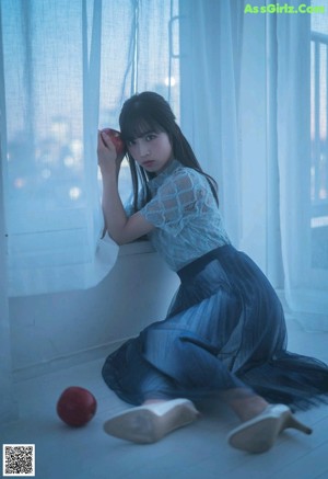 A woman in a blue dress is posing in front of a window.