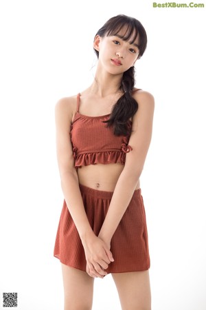 A woman in a brown top and shorts leaning against a wall.