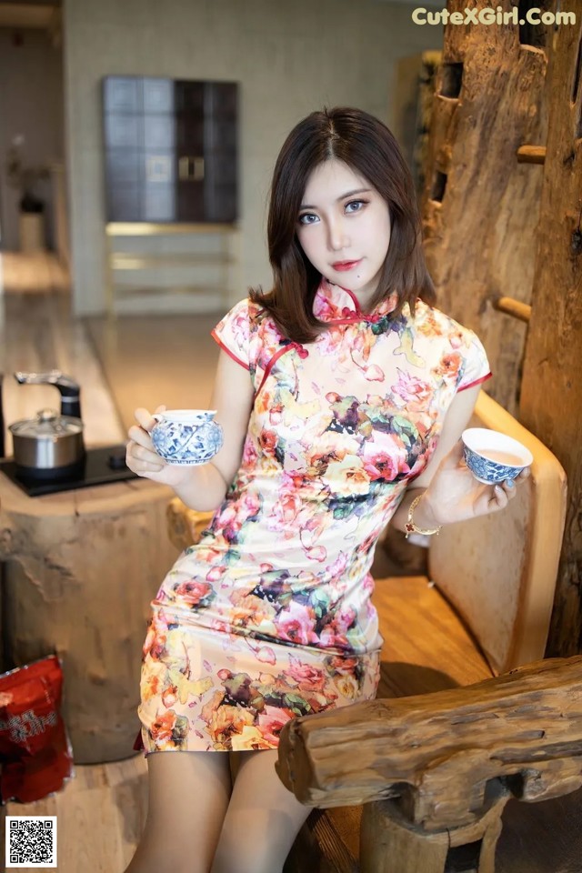 A woman in a floral dress holding a cup of tea.