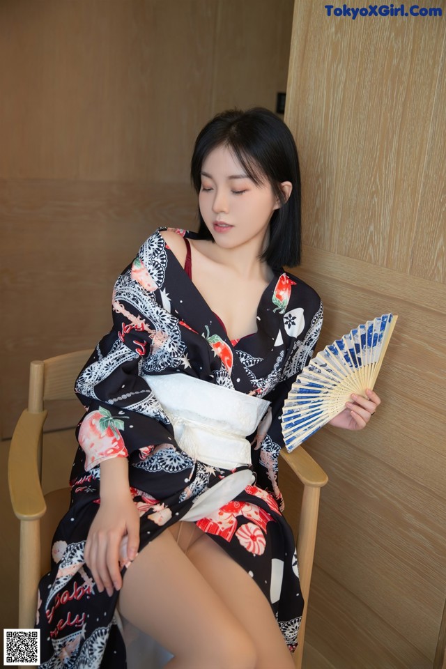 A woman in a kimono sitting on a chair holding a fan.