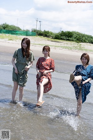 Three women sitting on a wall looking out at the ocean.