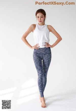 A woman in a white tank top and blue leggings holding a purple ball.