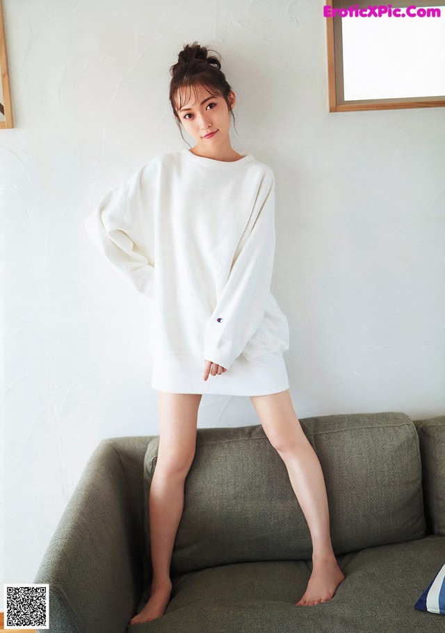 A woman sitting on a couch wearing a white sweatshirt dress.