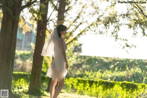 A woman in a white dress standing next to a tree.