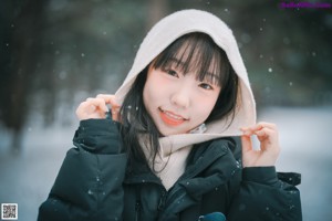 A woman standing in the snow wearing a scarf and jacket.