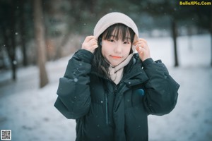 A woman in a black jacket and orange bikini sitting in the snow.