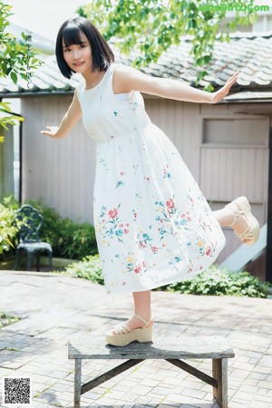 A woman standing in front of a white wall wearing a gray skirt.