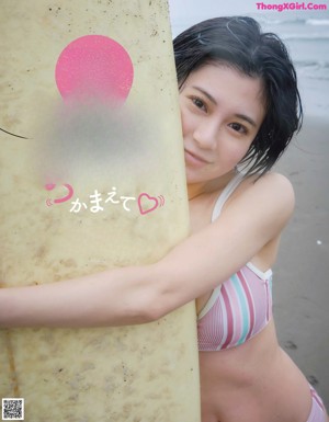 A woman in a bikini sitting on a surfboard next to a book shelf.