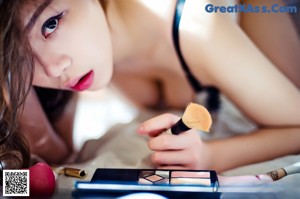 A woman laying on a bed with a makeup brush in her hand.