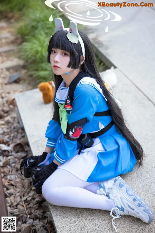 A woman in a blue and white outfit sitting on a bench.