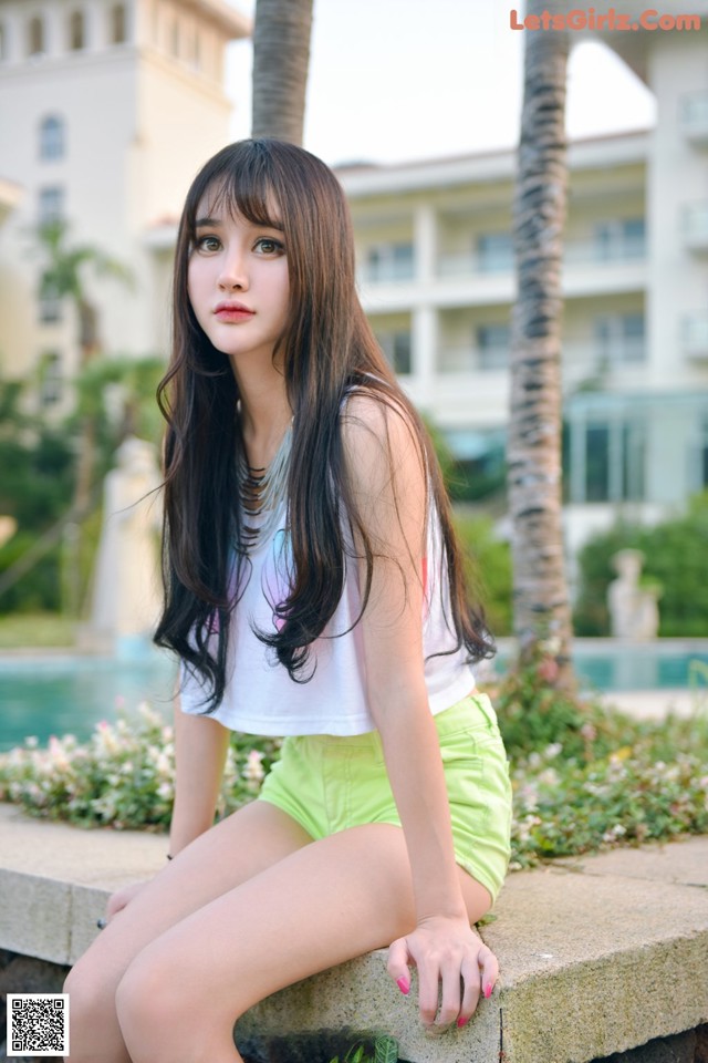 A young woman sitting on a stone wall next to a pool.