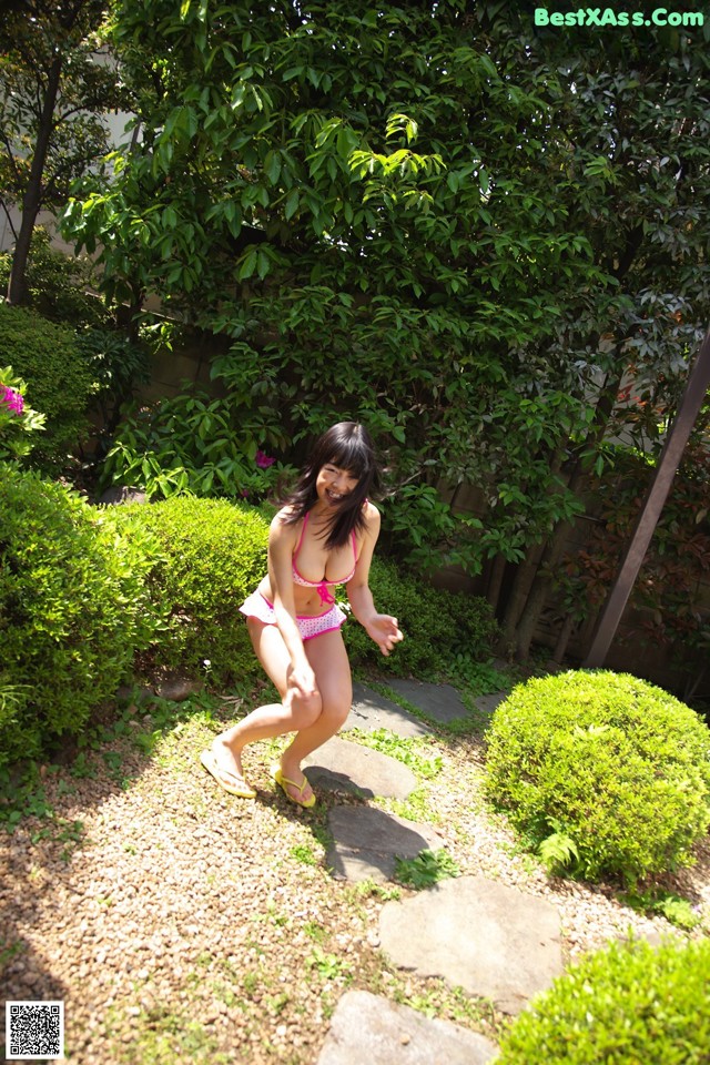 A woman in a pink bikini is walking through a garden.