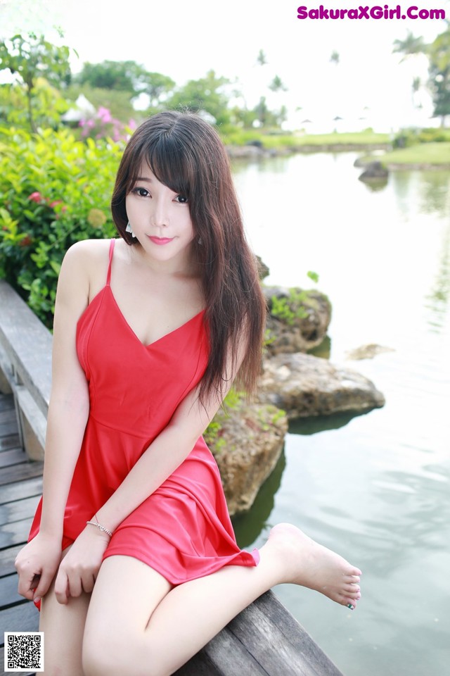 A woman in a red dress sitting on a wooden dock.