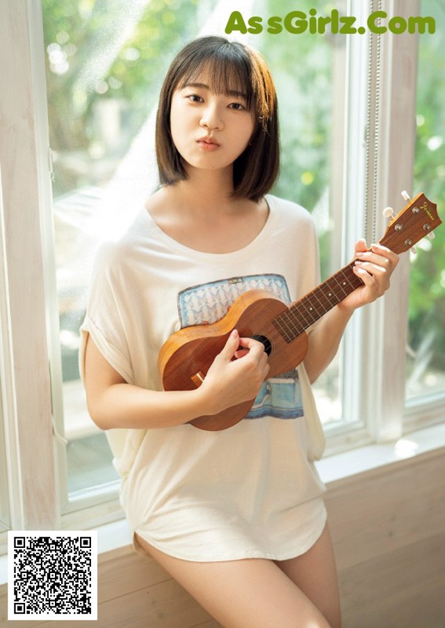 A young woman holding a ukulele in front of a window.