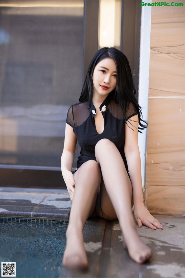 A woman in a black bathing suit sitting by a pool.