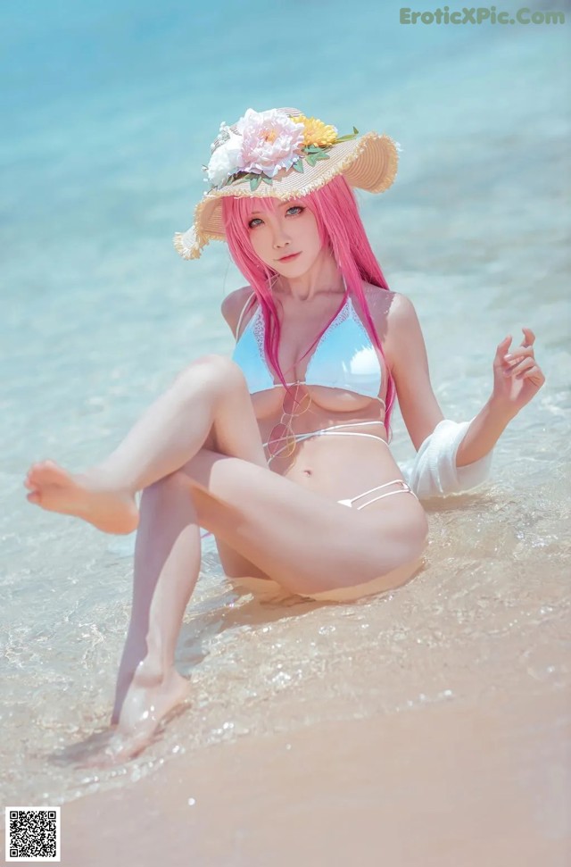 A woman in a bikini and hat sitting on the beach.