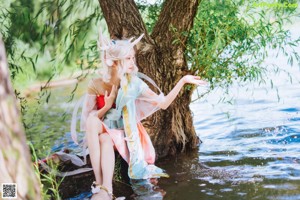 A woman sitting under a tree next to a body of water.