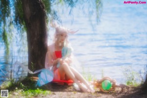 A woman sitting on the ground next to a body of water.
