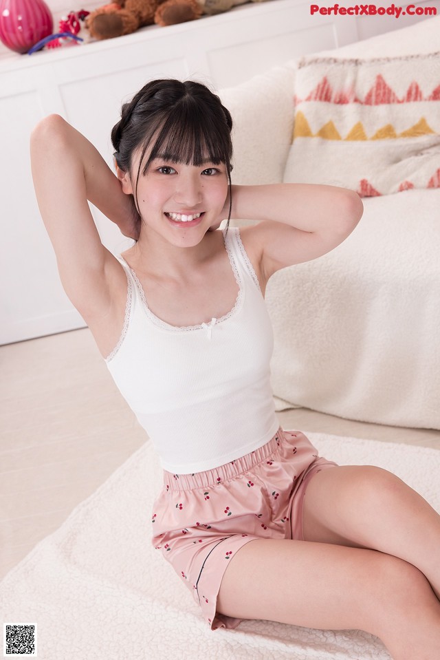 A woman in a white tank top and pink shorts sitting on a bed.