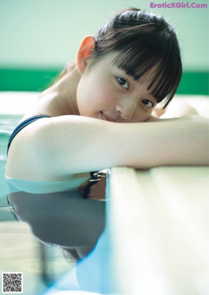 A woman in a black swimsuit standing next to a swimming pool.