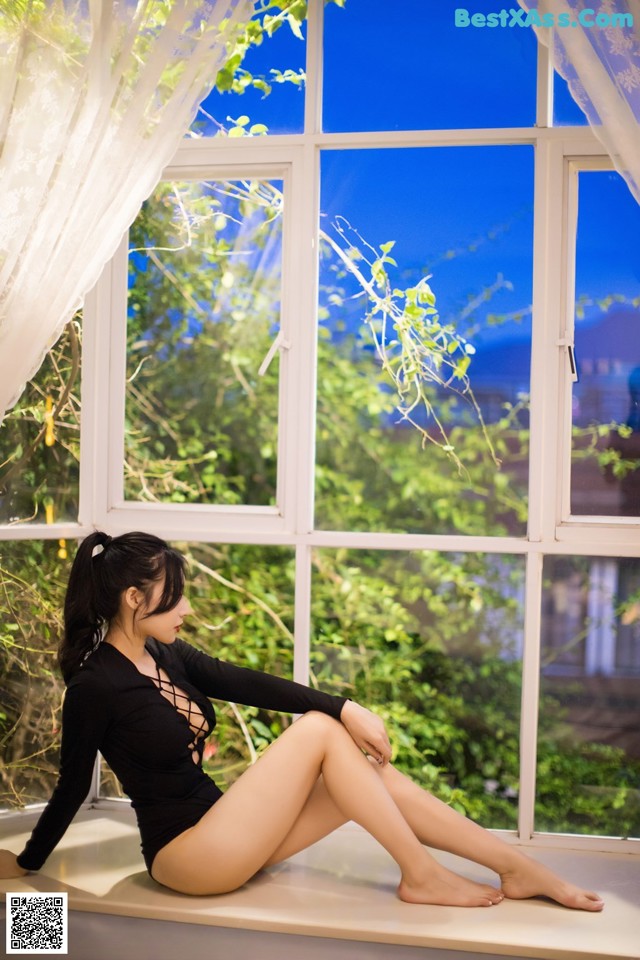 A woman sitting on a window sill in front of a window.