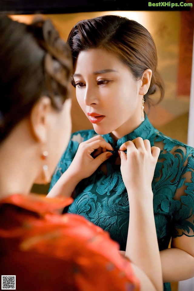 A woman putting on a green dress in front of a mirror.