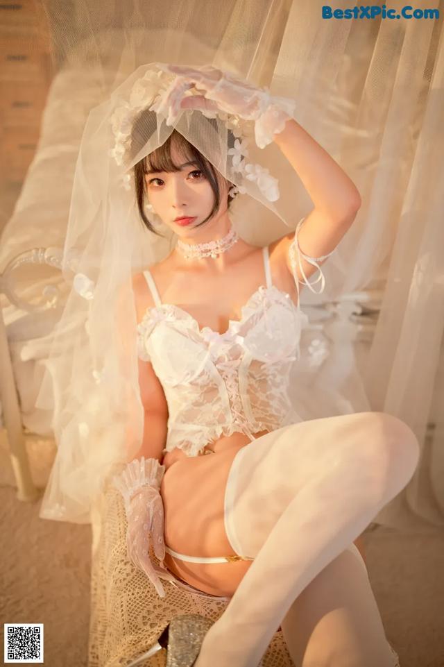 A woman in a white lingerie sitting on a bed.