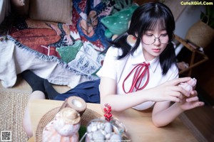 A woman in a white shirt and blue skirt sitting on a bed.