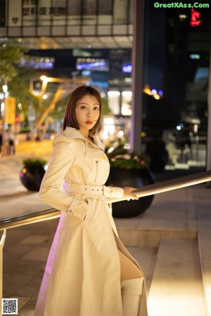 A woman in a white coat and pink lingerie posing for a picture.