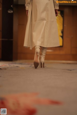 A woman in a white trench coat standing on a railing.