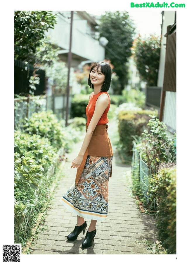 A woman in a brown top and patterned skirt standing on a sidewalk.