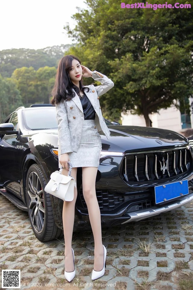 A woman standing in front of a black car.