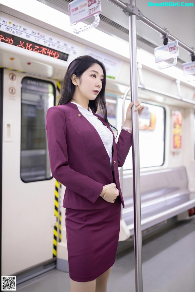 A woman in a purple suit standing on a subway train.