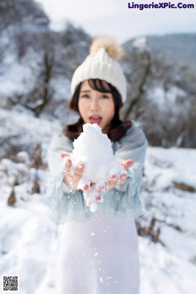 A woman in a white hat holding a snow ball in her hands.