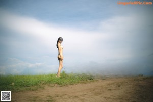 A naked woman standing on top of a lush green field.