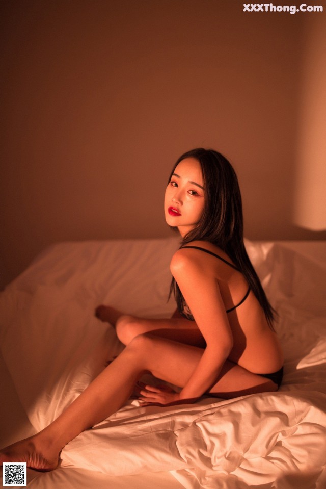 A woman sitting on a bed in a black lingerie.