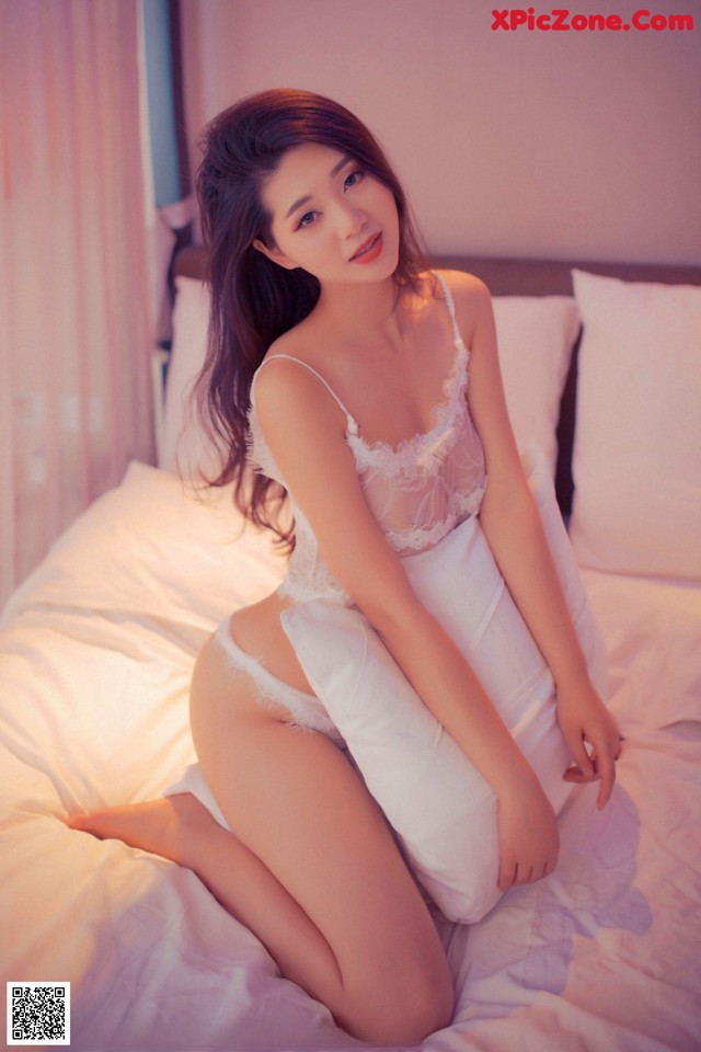 A woman in a white lingerie sitting on a bed.