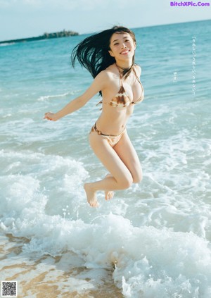 A woman in a black bathing suit sitting on a rock.