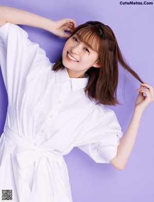 A woman in a white shirt dress sitting on a purple background.