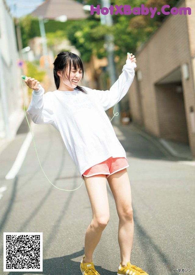 A woman in a white shirt and pink shorts is holding a skipping rope.