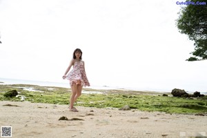 A woman in a floral dress standing on a beach.