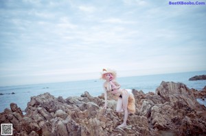 A woman with pink hair wearing a straw hat on the beach.