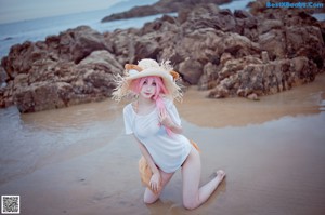 A woman with pink hair wearing a straw hat on the beach.