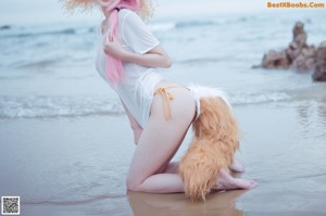 A woman in a bikini and hat standing on a rocky beach.