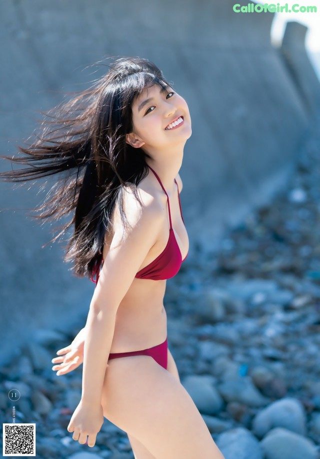 A woman in a red bikini standing on a rocky beach.