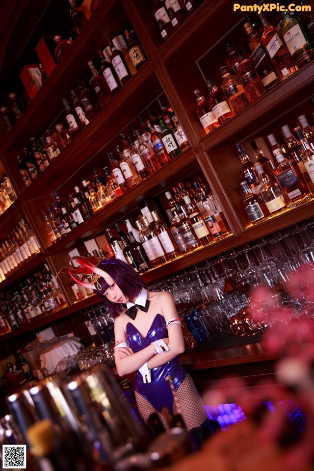 A woman in a blue dress standing in front of a bar.