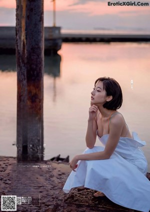 A woman in a white dress standing in front of a window.