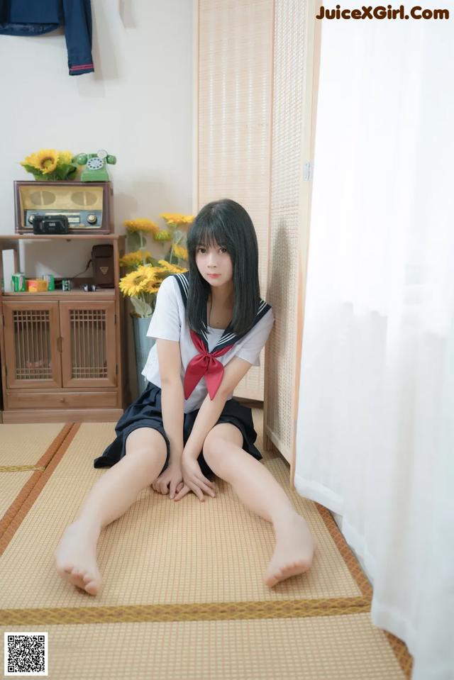 A woman in a school uniform sitting on the floor.