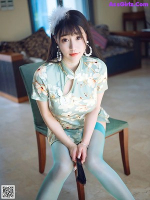 A woman in a green dress and white high heels leaning against a wall.